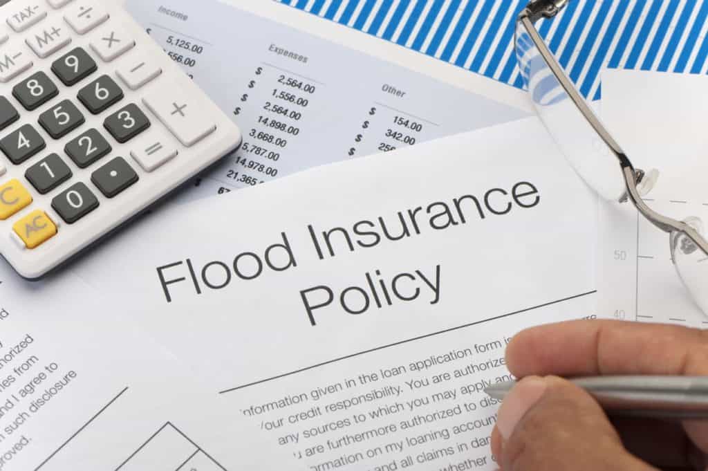 Close up of Flood insurance policy Form with pen, calculator and writing hand
